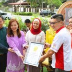 Group presenting an award certificate outdoors near a signboard, Canning Dim Sum, Kinta