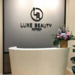 Reception desk with flowers below wall logo, Luxe Beauty Retreat, Petaling