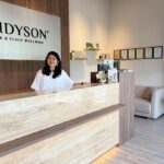 Receptionist smiling behind counter in wellness clinic lobby, Midyson Hair & Scalp Wellness, George Town