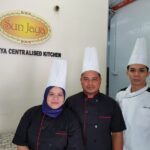 Kitchen staff in chef uniforms posing by wall sign, Sun Jaya Cafe And Catering, Tiada Maklumat